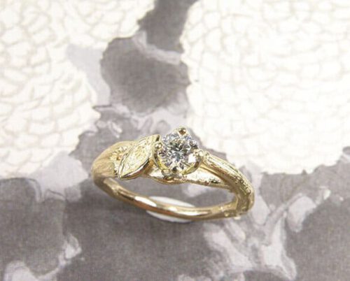 Verlovingsring 'Boomgaard'. Geelgouden ring overkruist takje met blaadje met 0,34 ct diamant. Engagement ring 'Orchard'. Yellow golden ring with twig, leaf and 0,34 crt diamond. Uit het Oogst atelier Amsterdam.