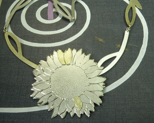 Zilveren Zonnebloem collier met geelgouden details en handgravure. Silver Sunflower necklace with yellow gold details and hand engravings. Uit het Oogst goudsmid atelier. Made in the Oogst goldsmith studio.