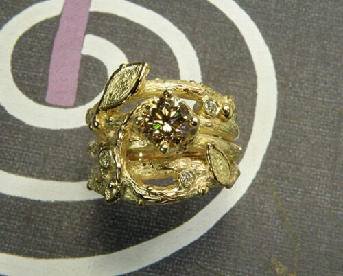 Verlovingsring 'Boomgaard'. Geelgouden twijgjes ring met blaadjes, besjes en een licht bruine diamant. Engagement ring 'Orchard'. Yellow golden ring with twigs, leafs, berries and a light brown diamond. Oogst goudsmeden Amsterdam.
