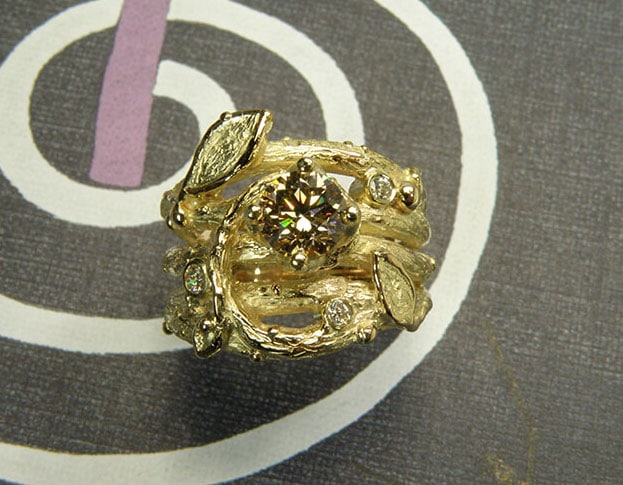 Verlovingsring 'Boomgaard'. Geelgouden twijgjes ring met blaadjes, besjes en een licht bruine diamant. Engagement ring 'Orchard'. Yellow golden ring with twigs, leafs, berries and a light brown diamond. Oogst goudsmeden Amsterdam.