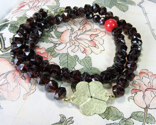 Armband van granaat in dubbele lengte met geelgouden klavertje en koraal. Bracelet made of garnet with a yellow golden clover and coral. Oogst goudsmeden Amsterdam.