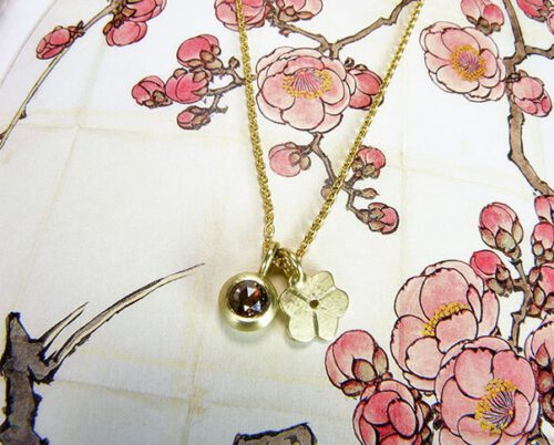 Geelgouden Japanse bloesem hanger en geelgouden hanger met bruine diamant. Necklace with a yellow golden Japanese blossom pendant and a yellow golden pendant with a brown diamond. Uit het Oogst atelier Amsterdam.