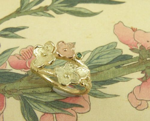 Verlovingsring 'In bloei'. Geelgouden takje met vrolijke bloemen en een groene diamant. Engagement ring 'In bloom'. Yellow golden twig with beautiful flowers and a green diamond. Uit het Oogst atelier Amsterdam.