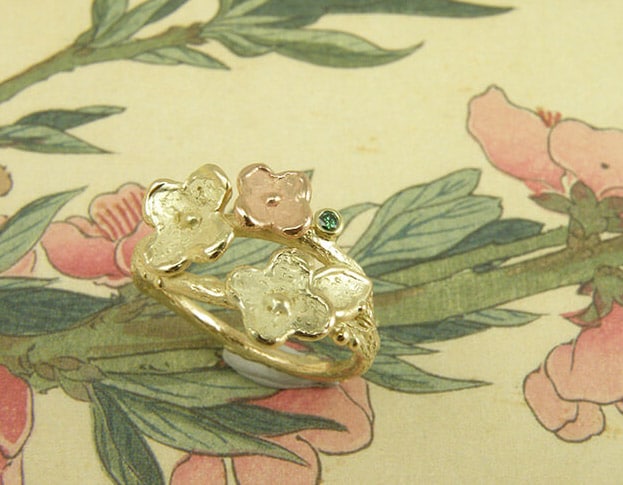 Verlovingsring 'In bloei'. Geelgouden takje met vrolijke bloemen en een groene diamant. Engagement ring 'In bloom'. Yellow golden twig with beautiful flowers and a green diamond. Uit het Oogst atelier Amsterdam.