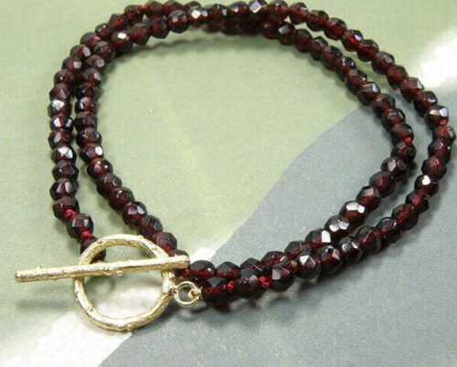 Armband 'Boomgaard' takjes sluiting vervaardigd van eigen goud gecombineerd met gefacetteerde granaat uit een erfstuk. Bracelet ‘Orchard’ twig clasp made of heirloom gold combined with heirloom garnet. Uit het Oogst atelier Amsterdam.