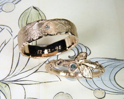 Trouwringen 'Erosie' & 'Boomgaard'. Roodgouden ring met een takje, 2 blaadjes en een ijsblauwe diamant. Roodgouden structuur ring met ijsblauwe diamant. Wedding rings 'Erosion' & 'Orchard'. Rose golden ring with a twig, 2 leafs and an ice blue diamond. Rose golden ring with structure and an ice blue diamond. Oogst goudsmeden Amsterdam.