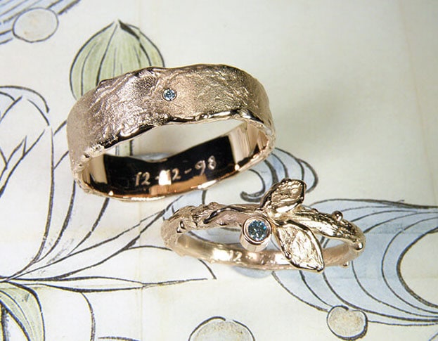 Trouwringen 'Erosie' & 'Boomgaard'. Roodgouden ring met een takje, 2 blaadjes en een ijsblauwe diamant. Roodgouden structuur ring met ijsblauwe diamant. Wedding rings 'Erosion' & 'Orchard'. Rose golden ring with a twig, 2 leafs and an ice blue diamond. Rose golden ring with structure and an ice blue diamond. Oogst goudsmeden Amsterdam.