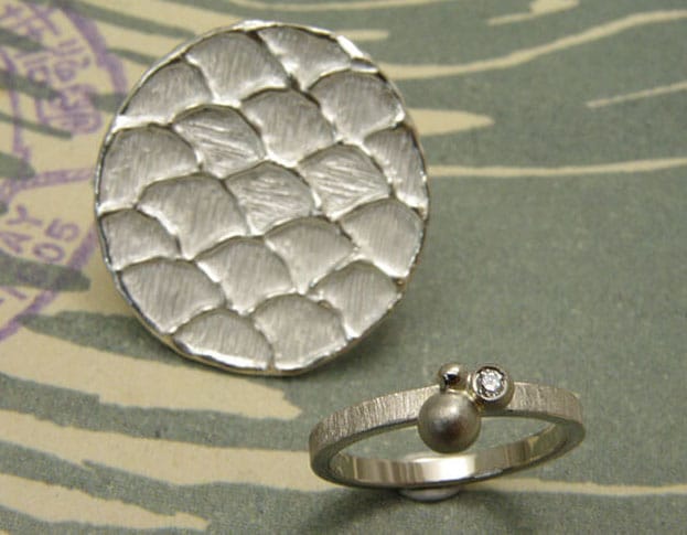 Trouwring 'Bessen' en speld 'Golf'. Witgouden ring met bolletjes en een diamant. Zilveren structuur speld met Japans golfpatroon. Wedding ring 'Berries' and pin 'Wave'. White golden ring with spheres and a diamond. Silver pin with Japanese wave pattern. Uit het Oogst atelier Amsterdam.