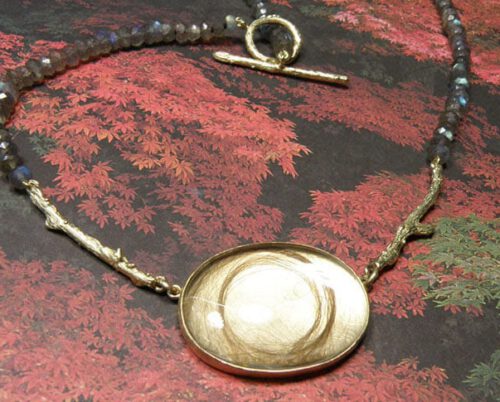 Labradoriet collier met geelgouden takjes en een lokje babyhaar onder bergkristallen. Geboorstesieraad. Labradorite necklace with a lock of baby hair underneath the quartz. Birth present. Oogst Amsterdam ontwerp & creatie.