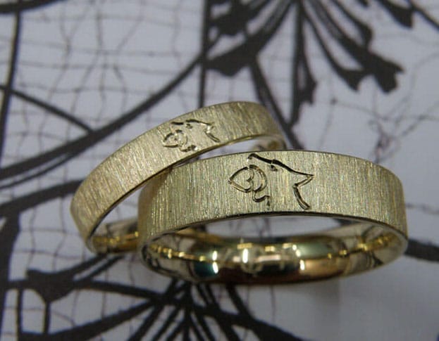 Hand engraved wedding rings 'Lineair'. Yellow golden wider ring with a wolf and heart symbol.