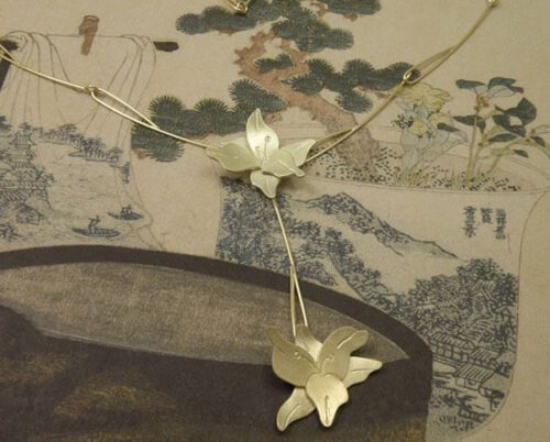 Geelgouden lelies bungelend aan elegante handgemaakte draadschakels. Yellow golden necklace with lillies and handmade chain. Oogst Amsterdam.