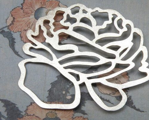 'In bloei' speld met zilveren ranonkel. 'In bloom' pin with silver flower. Uit het Oogst atelier Amsterdam.