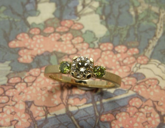 Verlovingsring 'Eenvoud'. Geelgouden ring met een 0,40 crt diamant en 2x 0,08 crt groene diamanten. Engagement ring 'Simplicity'. Yellow golden ring with a 0,40 crt diamond and 2x 0,08 crt diamonds. Uit het Oogst atelier Amsterdam.