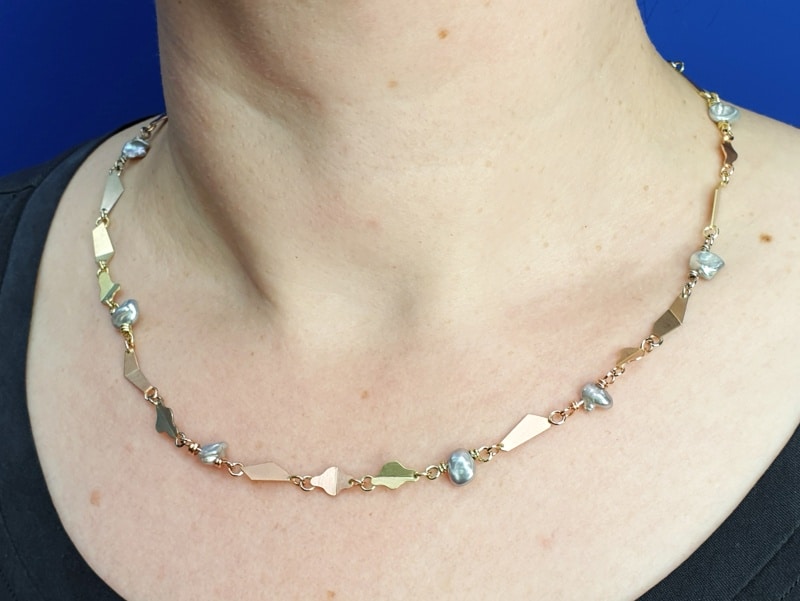Collier 'Vouwen' in roodgoud, geelgoud, witgoud en roségoud met grijze keshi parels. Ontwerp van Oogst goudsmid in Amsterdam uit de Amorf vs Kristallijn collectie.