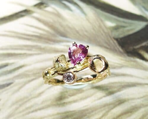 Geelgouden 'Twist' ring met een roségouden perzik, een kristal en 0,65 crt peergeslepen roze korund en 0,11 crt diamant brown . Ontwerp van Oogst goudsmid in Amsterdam voor de Amorf vs Kristallijn collectie.