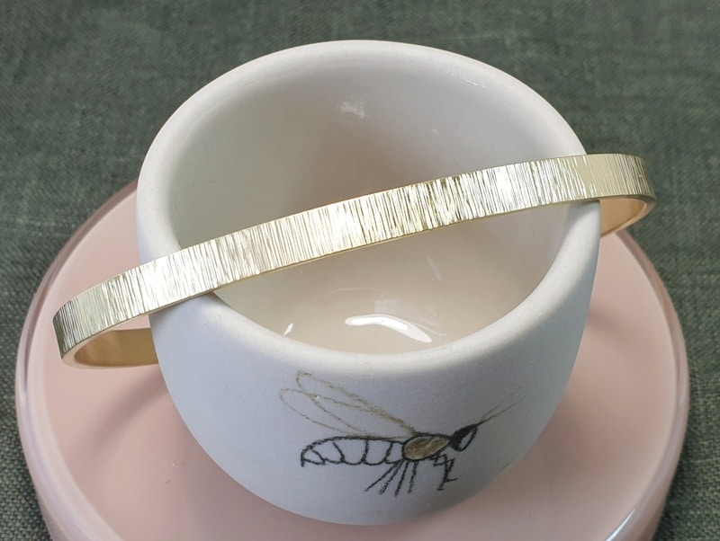 Yellow golden cuff bracelet Rhythm with stripey hammering and a brown diamond. Design by Oogst Jewellery in Amsterdam