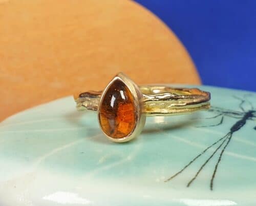 Assieraad 'Twist'. Ring met een druppelvormige oranje citrien in geelgoud vervaardigd. Met wat as onder de edelsteen verborgen. Uit het Oogst goudsmid atelier.
