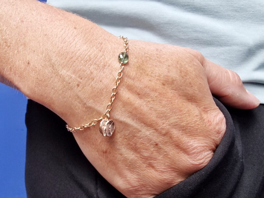 Roodgouden bedel armband met Mackintosh ornament en groene toermalijn. Verfijnd ontwerp van Oogst in Amsterdam. Om de pols.