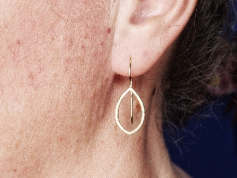 Blaadjes oorbellen in geelgoud. Met krul. Ontwerp van Oogst Sieraden in Amsterdam. Oorbel in het oor.