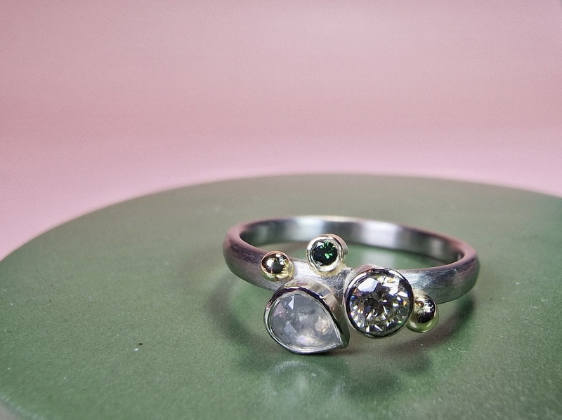 Verlovingsring Verzameling met drie diamanten in witgoud. Een grijze natural diamant peervorm, een cape briljant geslepen diamant en een groene diamantje. Met geelgouden besjes. Oogst Sieraden in Amsterdam. Maatwerk verlovingsring uit eigen atelier.