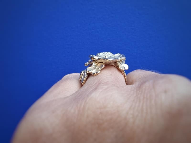 Geelgouden bloemen ring met speelse blaadjes en bloesemknop. Ring om de vinger gedragen, van de zijkant gezien. Ontwerp van Oogst Sieraden in Amsterdam