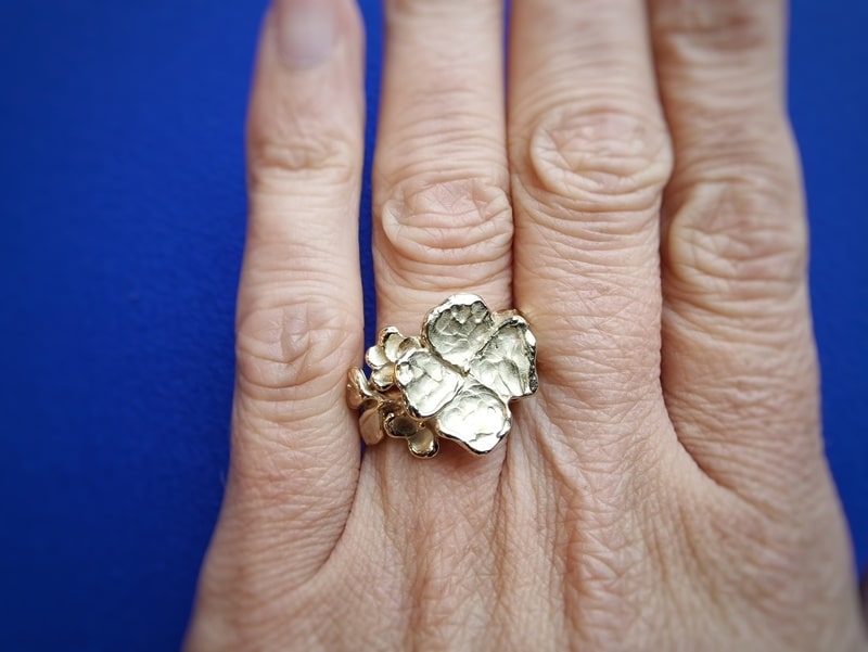 Geelgouden bloemen ring met speelse blaadjes en bloesemknop. Ring om de vinger gedragen. Ontwerp van Oogst Sieraden in Amsterdam