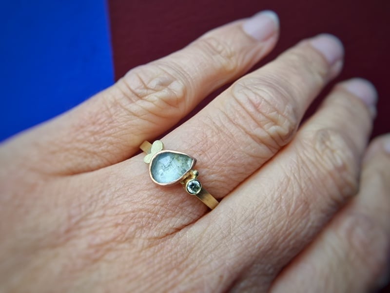 Geelgouden ring met mos Aquamarijn 1,07 ct free form in roodgouden zetting en 0,07 ct pistache diamant, met een geelgouden blaadje. Uit het Oogst goudsmid atelier. Om de vinger.