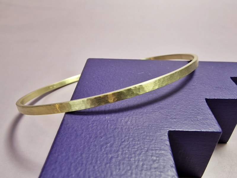 Geelgouden rinkelarmband met hamerslag verlopend van fijne naar streepjes hamerslag. Ovaal van vorm. Verfijnd sieraad uit het Oogst atelier. Uit de Ritme serie. Fijne hamerslag kant.
