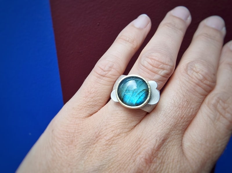 Zilveren edelsteenring met Labradoriet, in geelgoud gezet met wolk motief. Stoere robuuste zilveren ring. Oogst Goudsmeden in Amsterdam. Om de vinger gezien