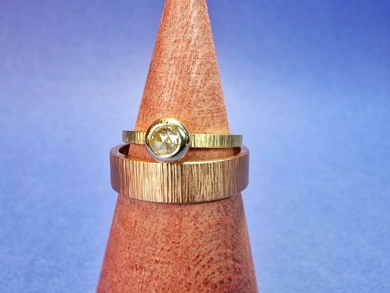 Trouwringen met spitse hamerslag. Geelgouden damesring met een roosgeslepen diamant. Roodgouden herenring. Uit het Oogst atelier.