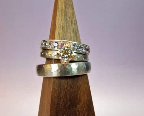 Witgouden trouwring hamerslag Ritme. Witgouden verlovingsring Ritme met stipjes en een 0,36 ct bruine diamant. Ernaast een witgouden eternity aanschuifring met spinel rondom. Handgemaakte trouwringen van Oogst Goudsmeden in Amsterdam.