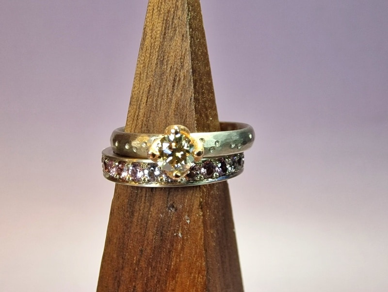 White gold engagement ring 'Rhythm' with a 0,36 ct diamond light brown with fine hammering and playful dots. Next to an eternity ring with spinel set pavé all around. Modern classic created in the Oogst studio.