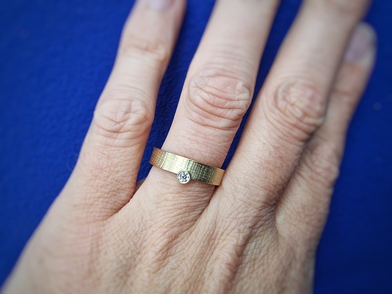 Linnen ring geelgoud met 0,10 ct diamant aan zijkant. Ring om de vinger gezien. Oogst Sieraden in Amsterdam.