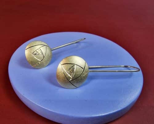 Geelgouden oorsieraden met een lange krul en eronder een grafische roosvorm geïnspireerd op het werk van Mackintosh.