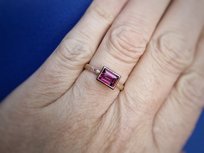 Roségouden ring met een rhodoliet en pink diamant ernaast gezet. Granaat is de geboortesteen van januari. Oogst Original. Om de vinger gedragen.