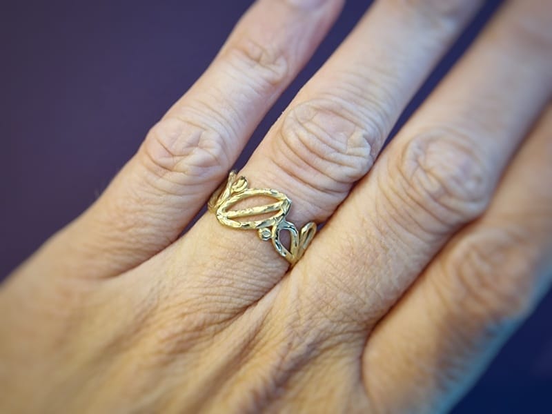 Mackintosh ring in geelgoud. Met open motieven van blaadjes en cirkels rondom. Uit het Oogst atelier. Om de vinger gezien.