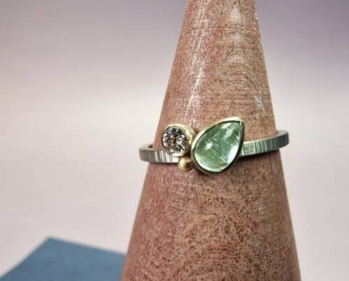 Verzameling ring in witgoud met spitse hamerslag en diamant, peervorm cabochon aquamarijn en een vrolijk besje. Eenmalig sieraad van Oogst Goudsmeden.